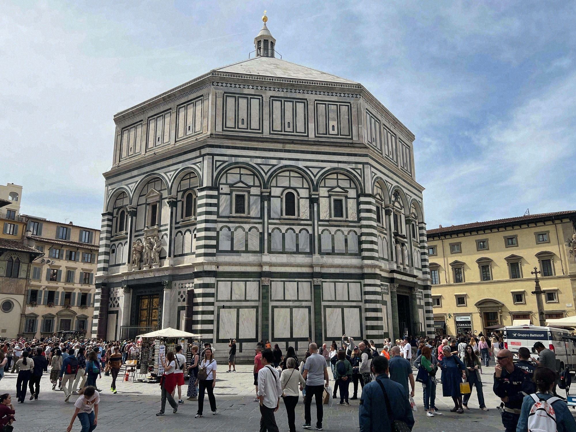 Das achteckige Baptisterium San Giovanni mit seiner charakteristischen gruen-weissen Marmorverkleidung und vergoldeter Kuppel, umgeben von Touristenmassen auf der Piazza del Duomo.
