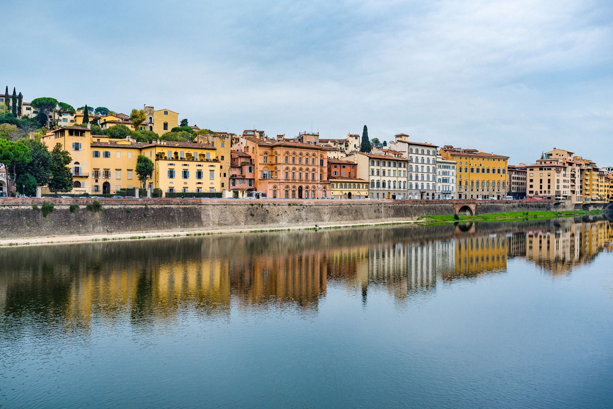 Blick auf das Oltrarno-Viertel mit typischen Florentiner Häusern und spiegelndem Arno-Fluss, charakteristische Stadtsilhouette mit Kirchturm.