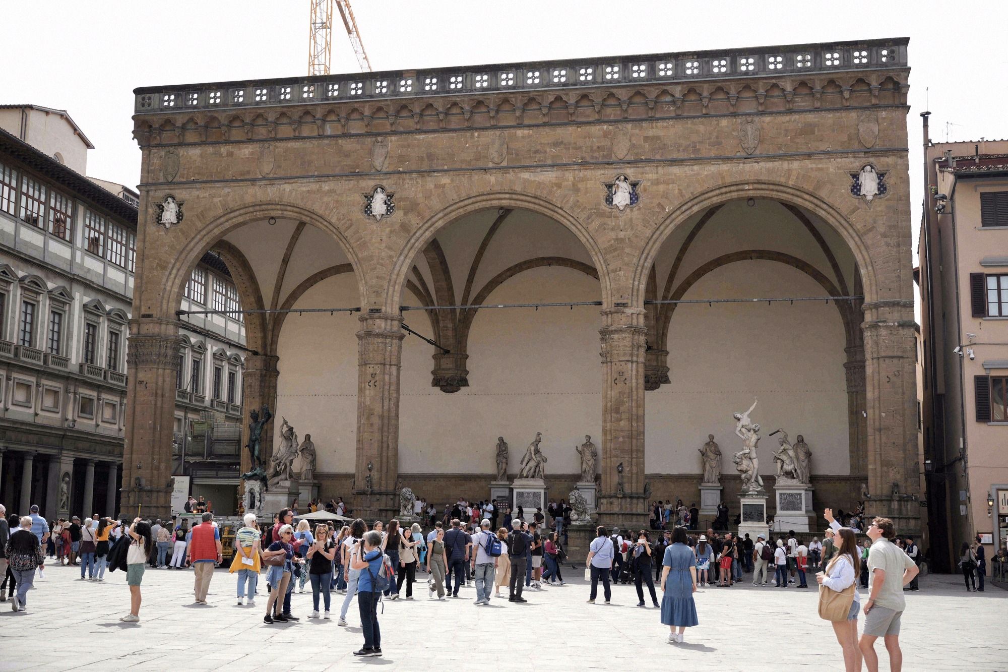 Die Loggia dei Lanzi an der Piazza della Signoria mit ihren drei grossen Rundboegen und den Skulpturen darunter, belebt von zahlreichen Touristen.